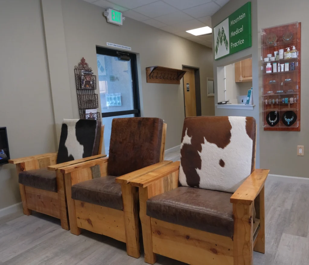 Mountain Medical Practice interior with cowhide chairs in waiting room, antique magazine wall rack, gift shop display case, reception window, western style coat hook wall mount, and door to ADA restroom
