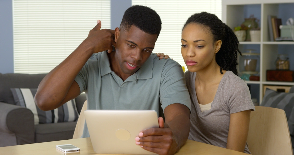 Youthful couple including male and female seated at laptop computer with male indicating neck pain during telemedicine session