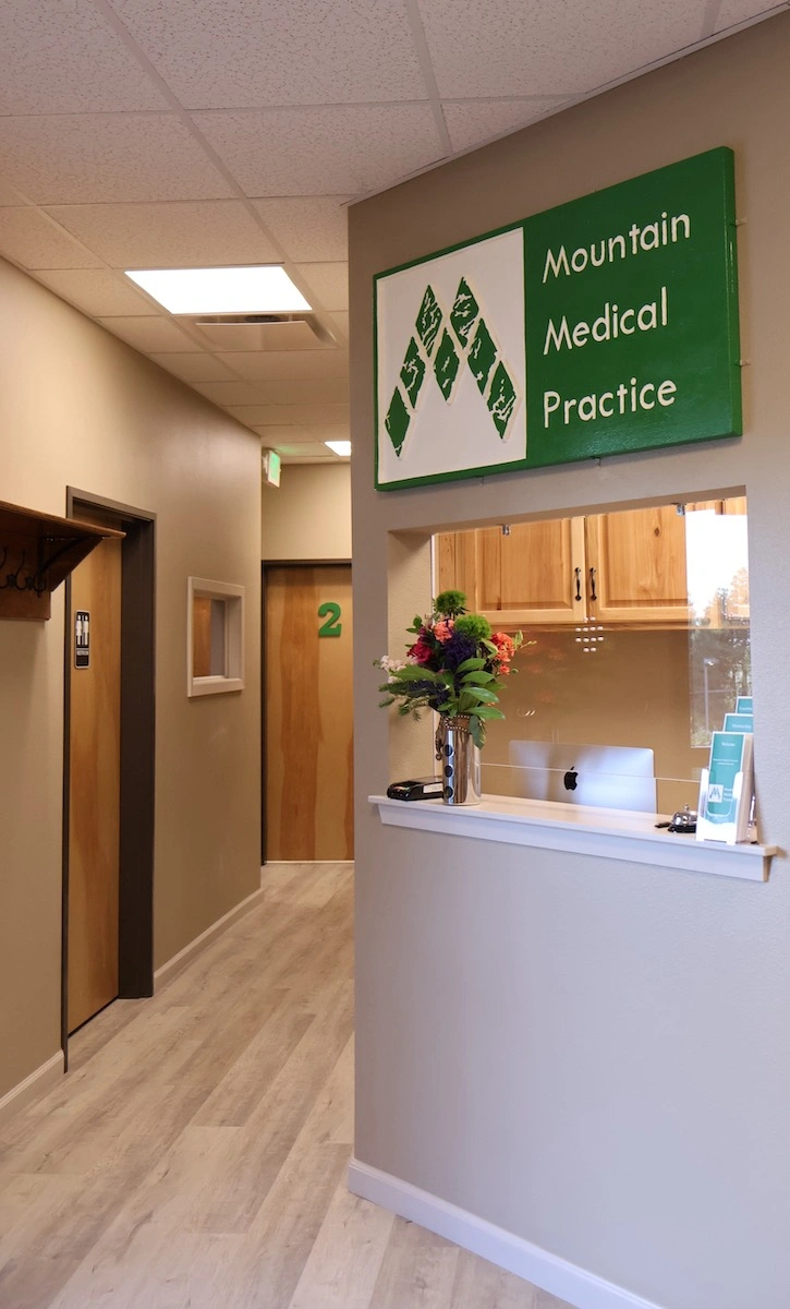 Mountain Medical Practice reception window with decorative flowers in silver vase and front hallway with western style coat hooks mounted on wall