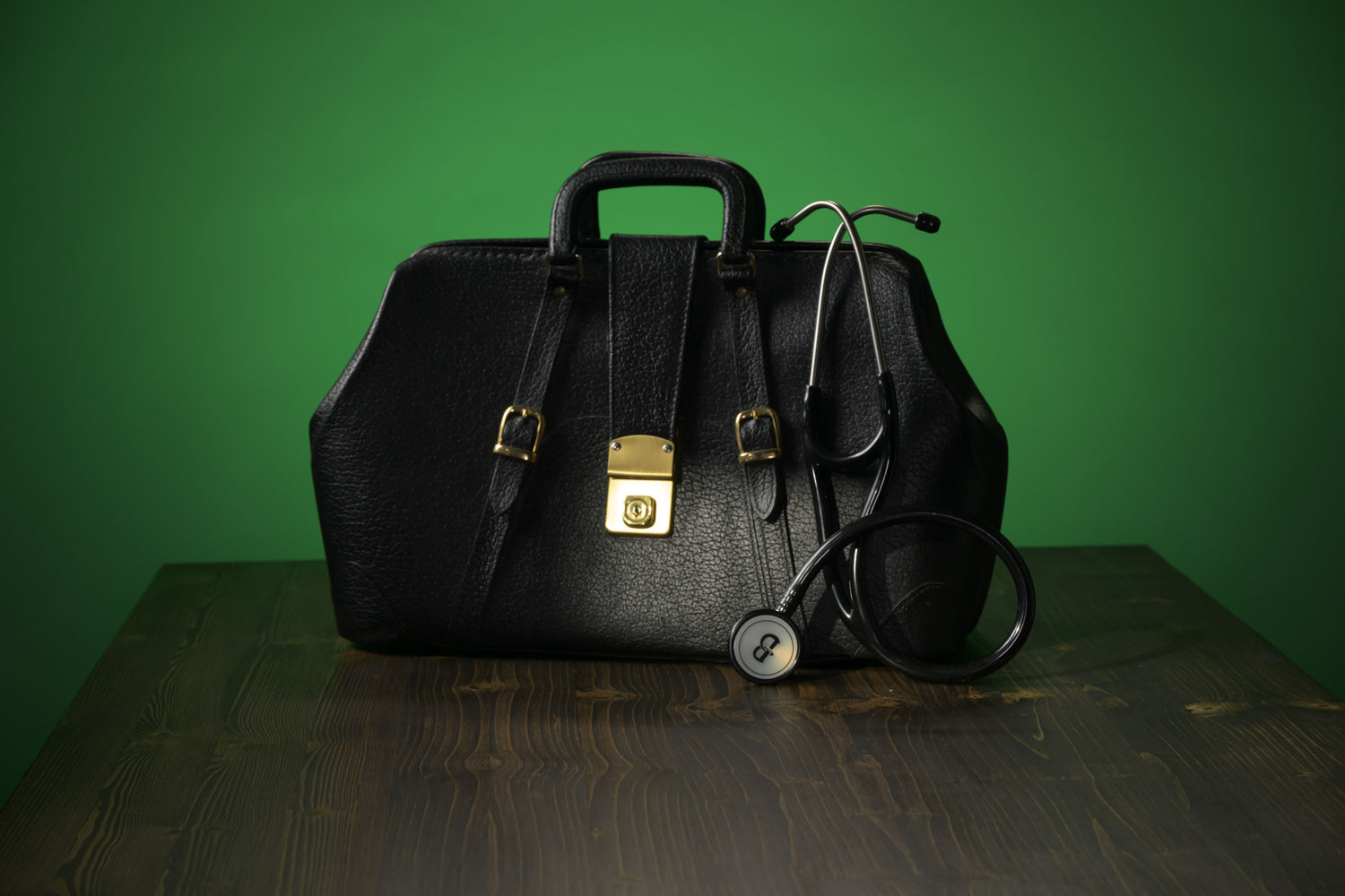 Vintage black medical doctor bag with stethoscope on green background
