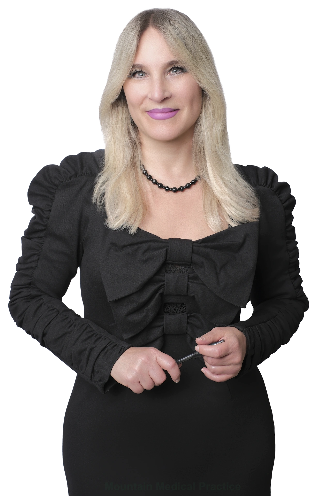 Dr. Maria Pirraglia in black Symphonie dress with bow accents and black beaded necklace standing holding pen in hands facing straight on