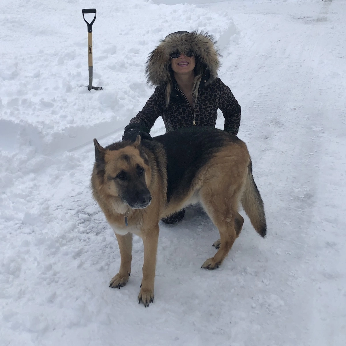Maria Pirraglia in leopard ski onesie with German Shepherd standing in the snow