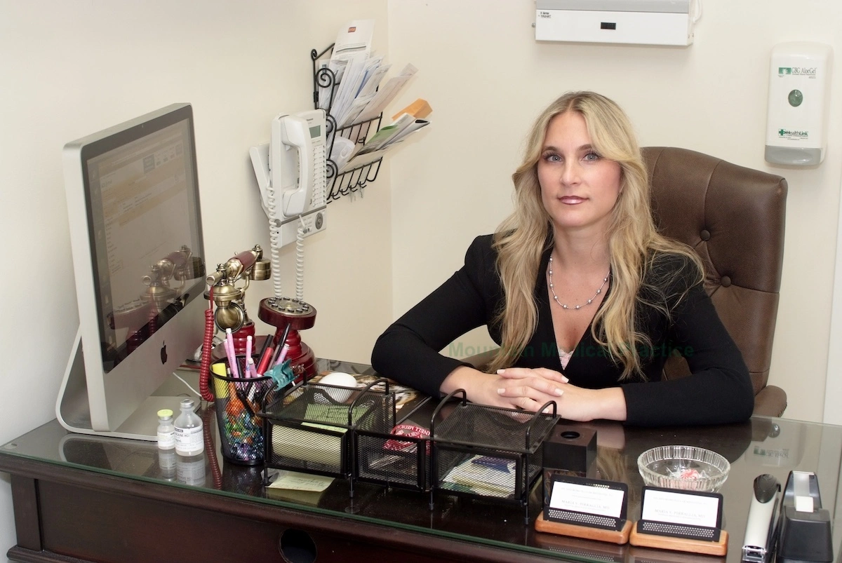 Dr. Maria Pirraglia in black business suit seated at desk with antique vintage telephone