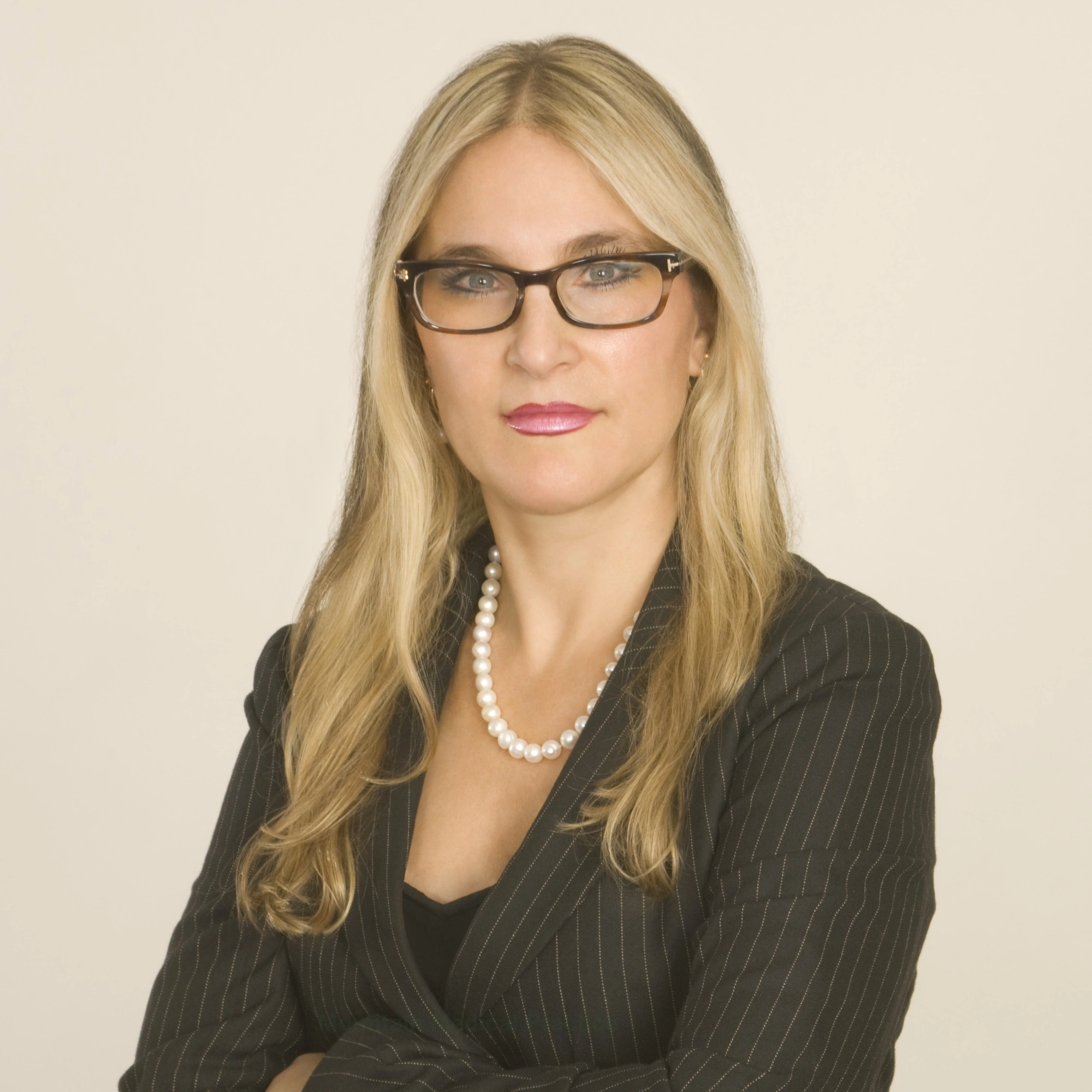 Dr. Maria Pirraglia in tortoise frame eyeglasses, white pearl necklace, and gray pinstripe suit facing straight on