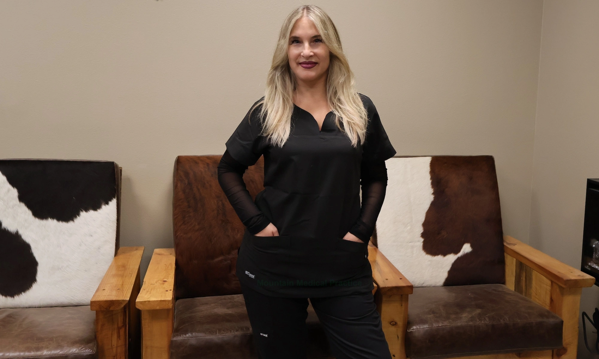 Dr. Maria Pirraglia in black Grey’s Anatomy scrubs in casual stance in front of rustic cowhide chairs in office waiting room