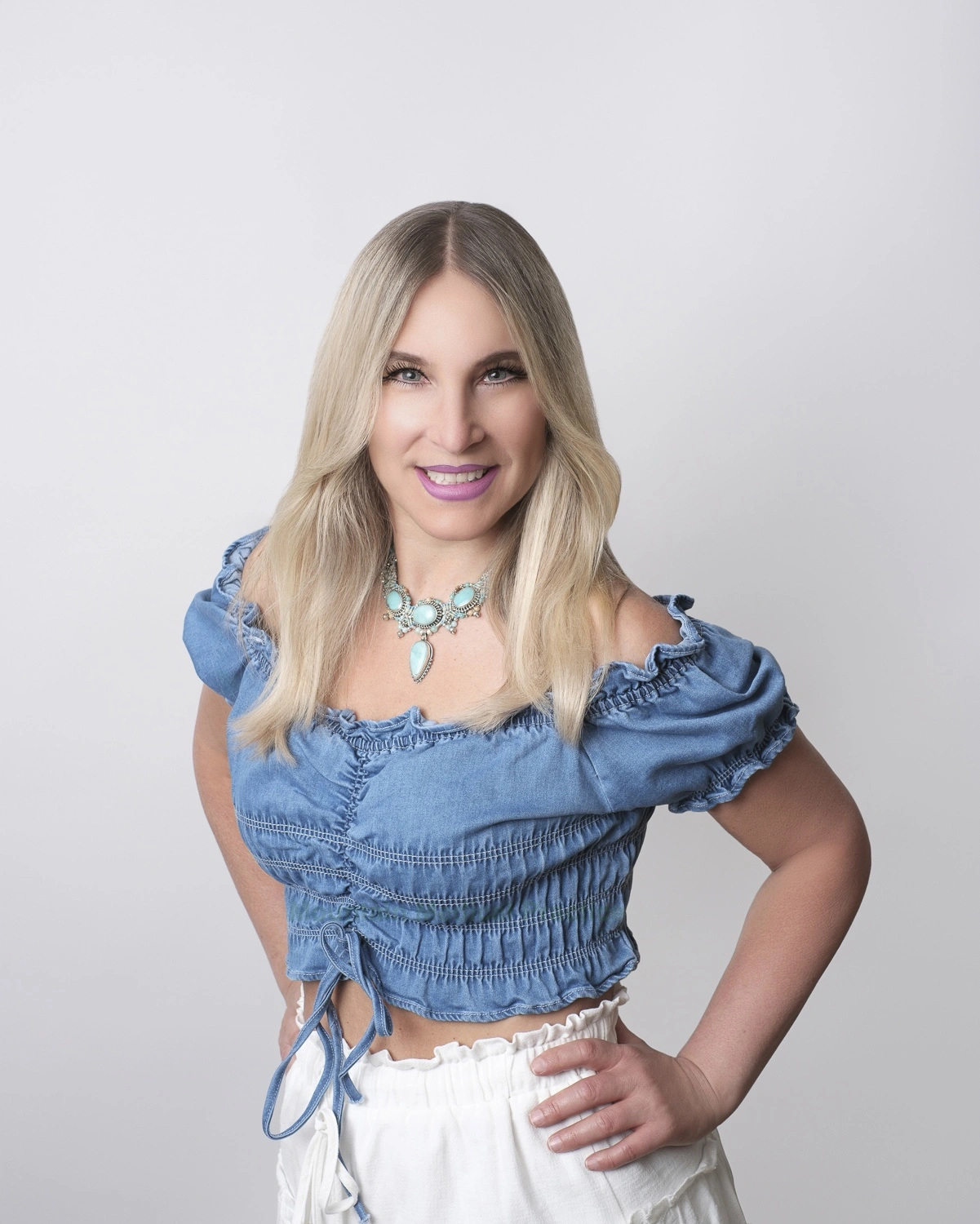 Maria Pirraglia in turquoise necklace, cropped denim top, white skirt