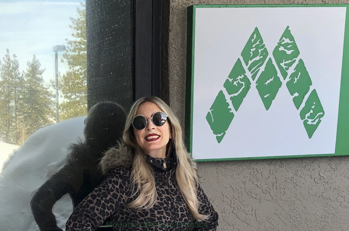 Dr. Maria Pirraglia in round wire framed sunglasses and leopard snowsuit standing in front of Mountain Medical Practice entrance