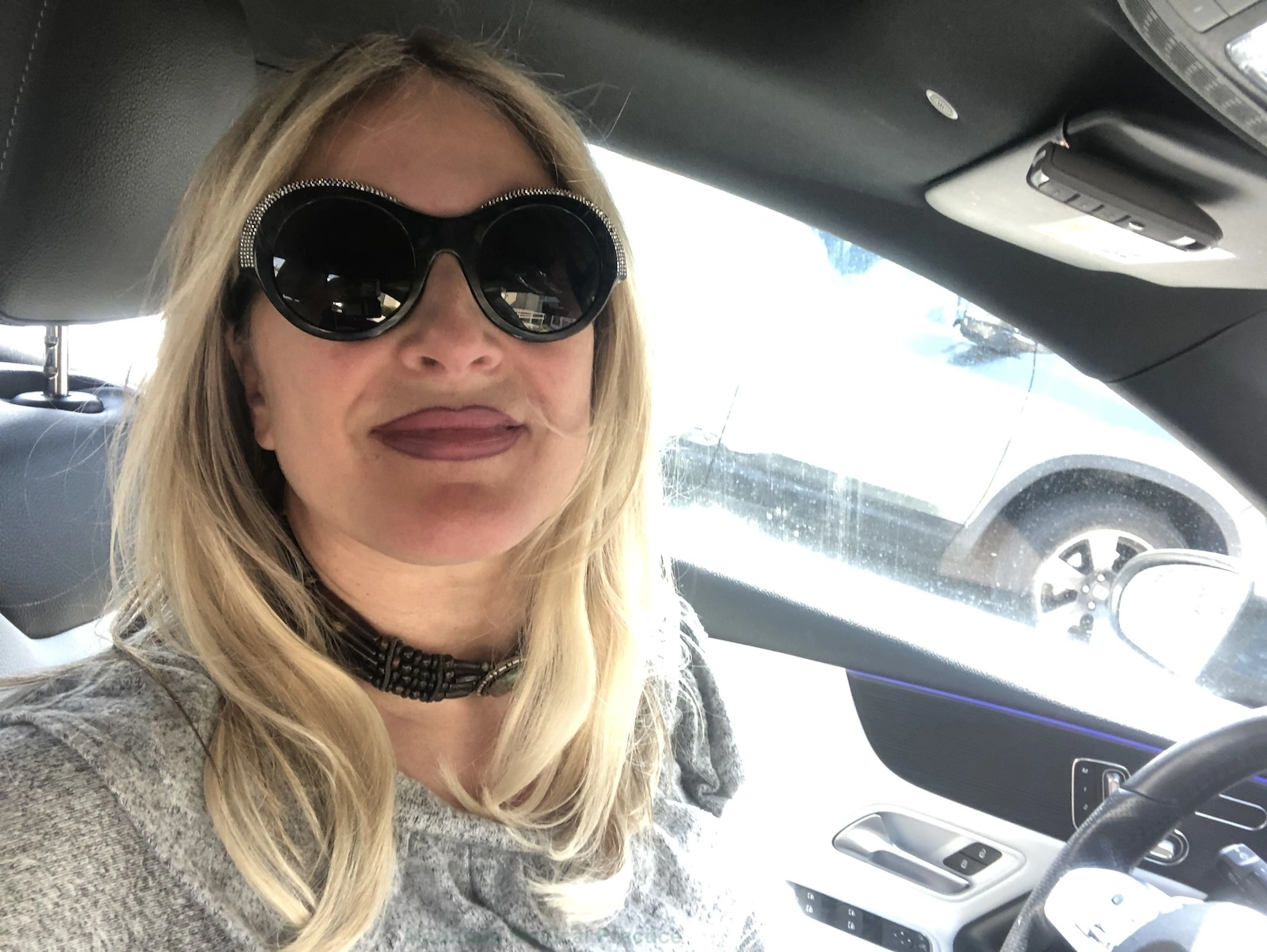 Maria Pirraglia wearing rhinestone sunglasses and brown bone choker casual selfie in car parked in Reno