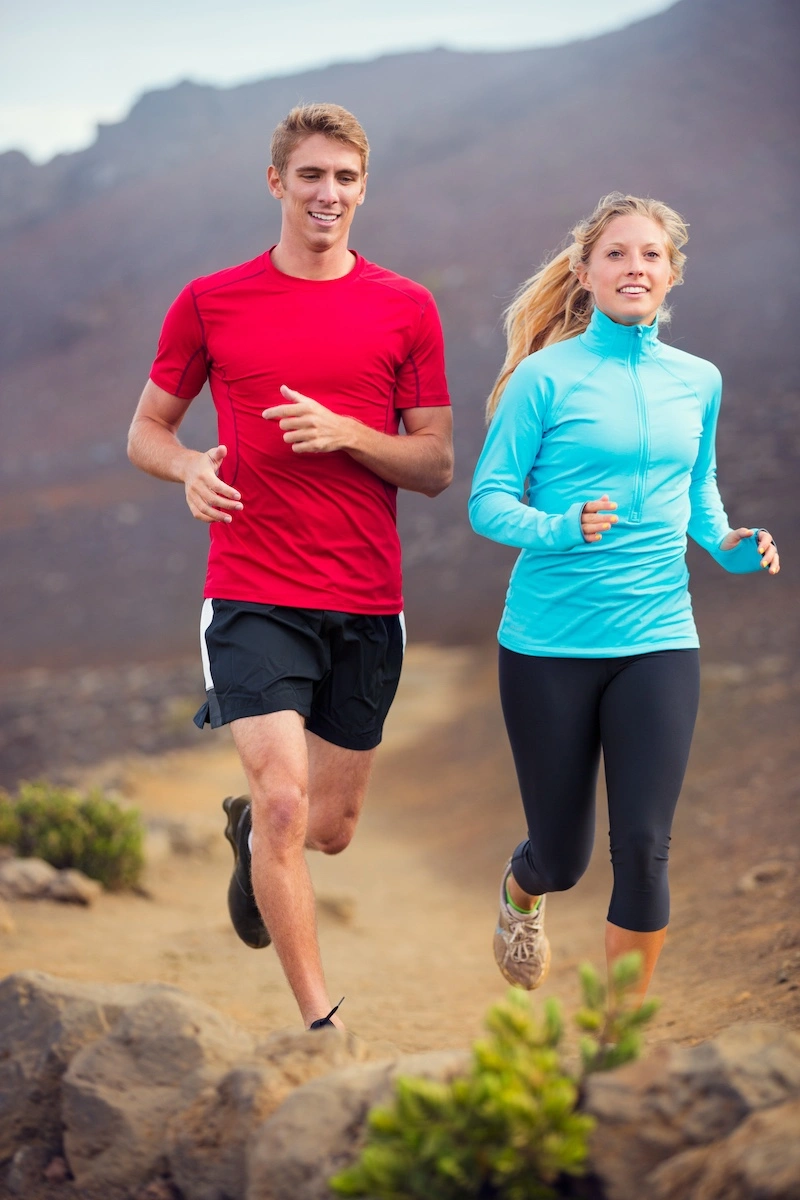 Athletic male and female in sports attire jogging on rocky dirt mountain trail