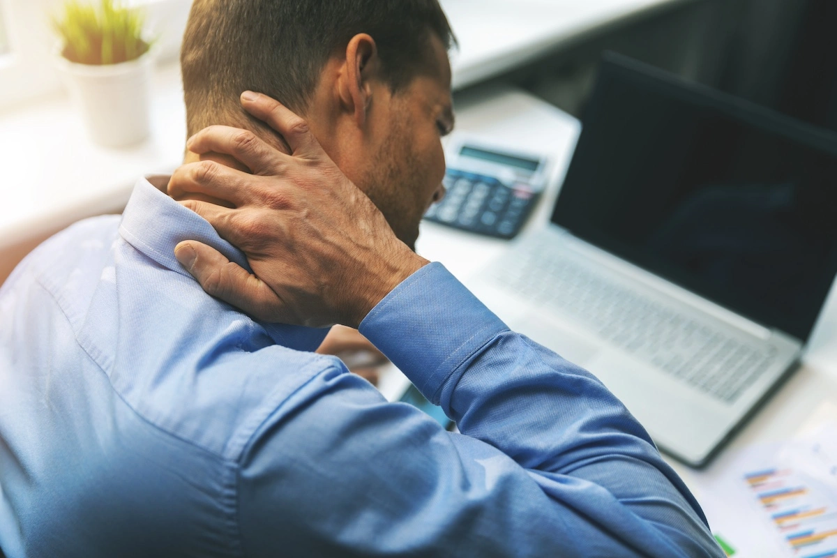 Male in business attire at laptop computer clutching neck in pain