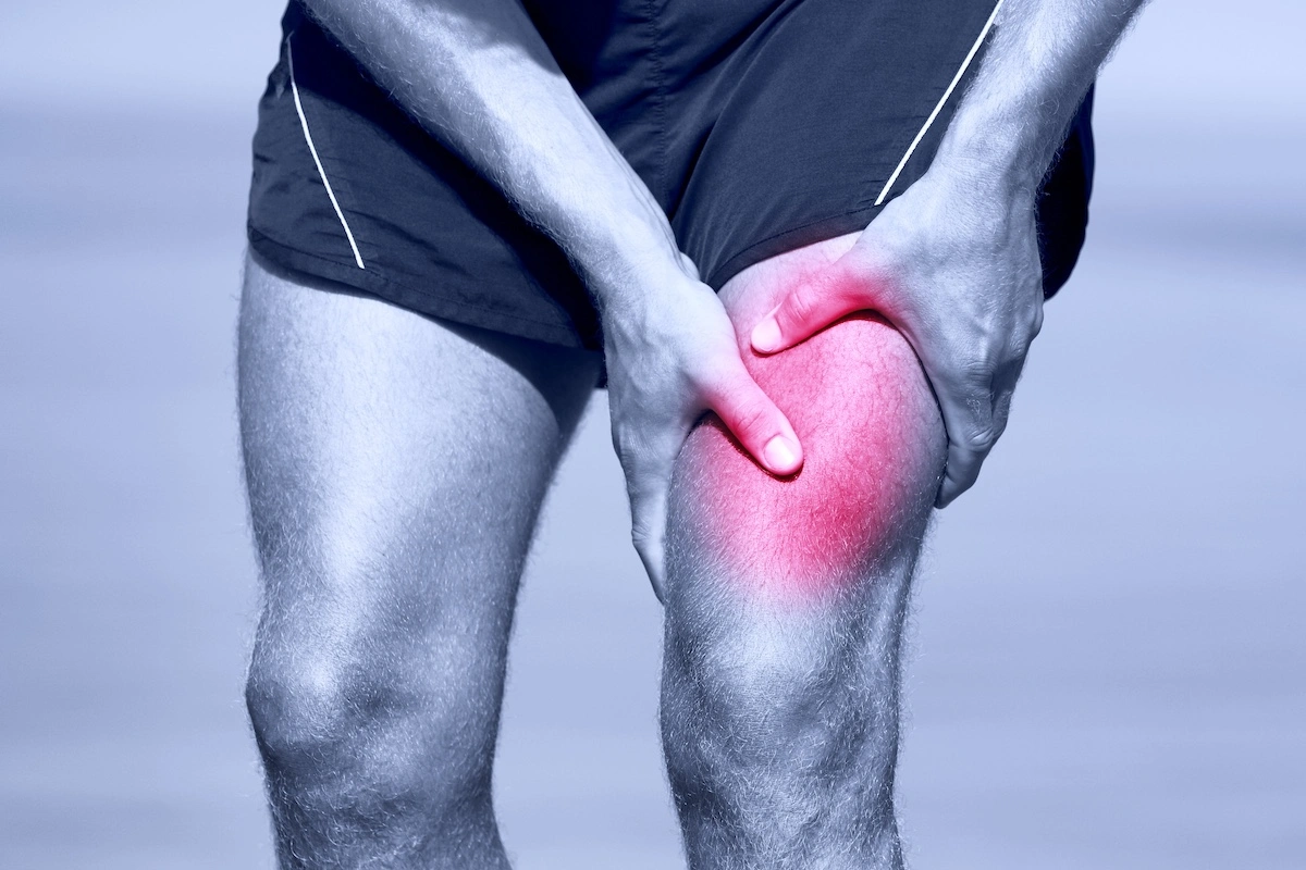 Athletic male in jogging shorts clutching thigh muscles in pain