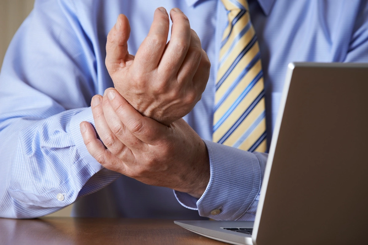 Male in business attire at laptop computer clutching wrist in pain